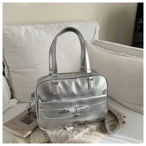 Close-up of silver Boston tote bag with bow detail and heart pendant on a soft knit rug