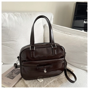Detail of a dark brown glossy leather handbag featuring a bow and heart pendant charm