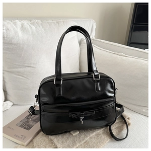 Close-up of black glossy leather tote featuring a bow detail and a small heart charm