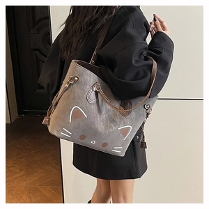 Detail of grey cat tote bag with brown handles worn on shoulder by a model indoors