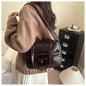 Detail view of brown shoulder bag with bow and silver heart pendant in lifestyle setting