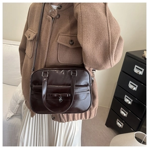 Detail of dark brown glossy tote bag with bow and heart pendant on a shoulder strap