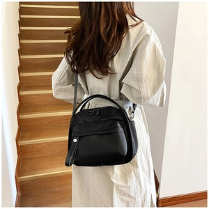 Detail of black nylon tote bag with curved handle and front zipper pocket on wood stairs