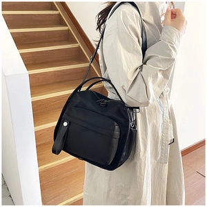 Detail of black nylon crossbody bag with silver hardware on a model with beige coat