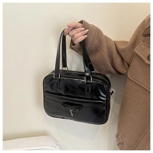 Detailed view of black patent leather shoulder bag with a bow and silver hardware charms
