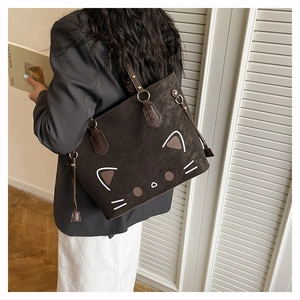 Detail of dark brown suede tote bag with white cat face illustration and metal strap buckle