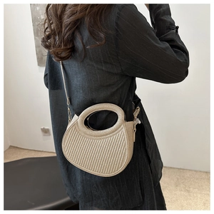 Detail view of beige half-moon straw bag with vertical texture and round cutout handle