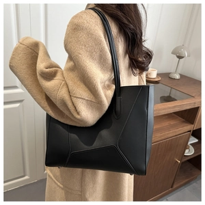 Detail of a minimalist black leather tote bag with protective metal rivets on the bottom