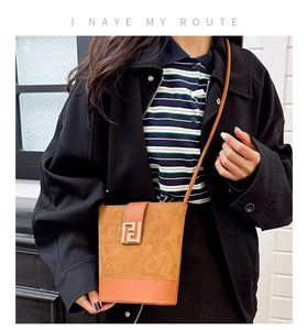 Detail of a brown patchwork crossbody bucket bag with suede texture and metal buckle