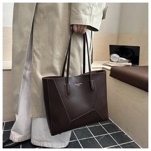 Detail of deep brown tote bag featuring minimalist gold-stamped logo and contrast stitching