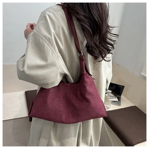 Detail of burgundy faux suede shoulder bag with adjustable silver buckle on a trench coat