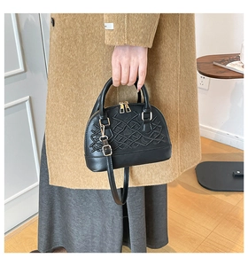 Detail of black shell bag featuring woven texture, gold dual zippers and leather handle