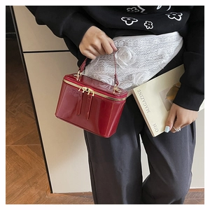 Detail of dark red patent leather handbag with dual gold zippers and glossy mirror finish