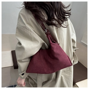 Detail of burgundy suede shoulder bag worn with a khaki coat showing elegant matte texture