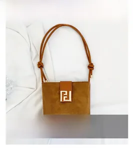 Detail of brown suede shoulder bag featuring a gold geometric buckle and knotted strap