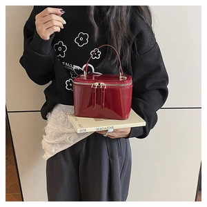 Gros plan d'un sac boîte en cuir verni bordeaux avec zips dorés porté par un mannequin