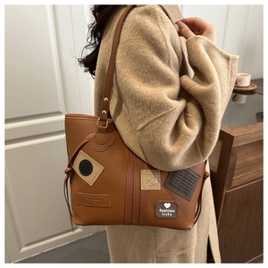 Detailed close-up of brown PU leather tote bag with fashion lucky patches and golden hardware