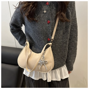 Detail view of a beige crescent moon bag featuring an elegant metal bow charm accessory