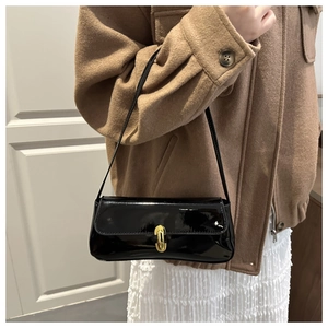 Detail of glossy black patent leather baguette bag with elegant gold metal clasp on model