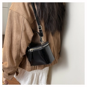 Close-up of black patent leather mini box bag with gold zipper and adjustable strap