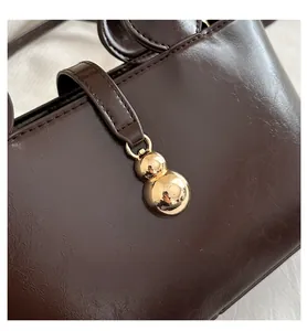 Detail of dark brown bucket bag with shiny leather texture and golden gourd pendant