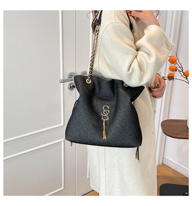 Close-up of black textured tote bag with golden S-logo, fringe tassel and chain strap