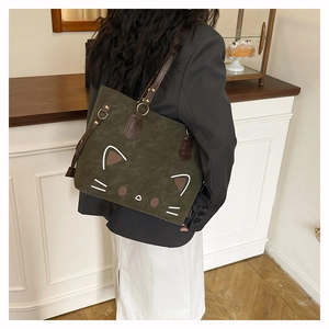 Detail of green suede tote bag with cartoon cat face and brown leather shoulder straps