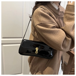 Glossy black patent leather baguette bag with a gold capsule buckle on a model shoulder
