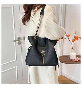 Detail der schwarzen Plissee-Tasche mit goldenem SS-Logo, Quaste und Kettengurt am Model