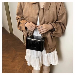 Detailed close-up of glossy black patent leather box bag with dual gold zippers and top handle