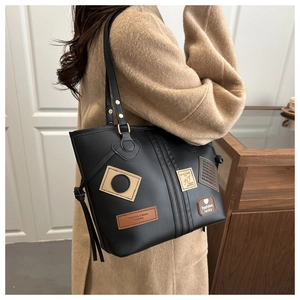 Detail of black PU leather tote bag with colorful patches and shoulder strap shown on model
