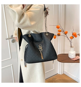 Detail of black tote bag featuring shimmering texture and golden chain with S logo tassel