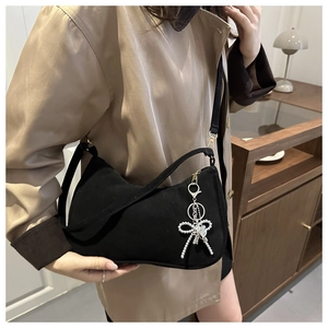 Dettaglio di una borsa a mezzaluna nera con ciondolo a fiocco argentato su modella