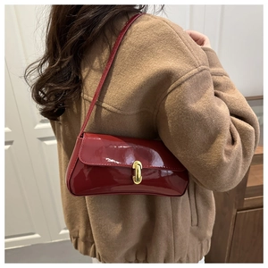 Close-up of wine red patent leather baguette bag with gold buckle on brown wool coat