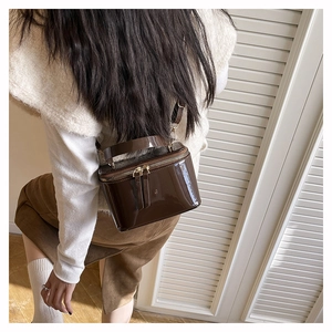 Detail view of a dark brown glossy patent leather box bag worn with an autumn outfit
