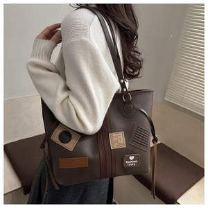Detailed view of dark brown faux leather tote with vintage patches on beige sweater