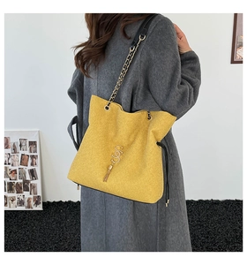 Détail du sac bandoulière jaune avec breloque lettre S dorée, pompon et bandoulière chaîne
