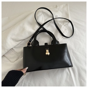 Detail of black matte leather shoulder bag with golden double ball charms and strap