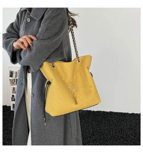 Detail of yellow tote bag with metallic S-pendant, tassel, and chain strap detail