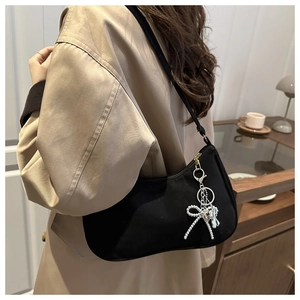 Detail of black nylon hobo bag with beaded bow charm and golden zipper on shoulder