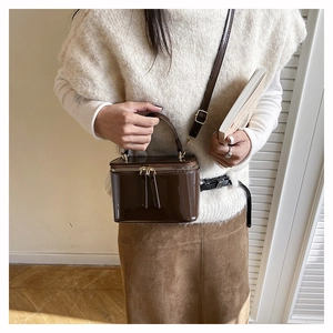Detail of a brown patent leather box bag with a glossy finish and dual zipper closure