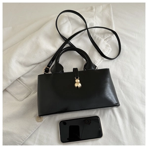 Glossy black faux leather bucket bag with gold ball charm and phone for size reference