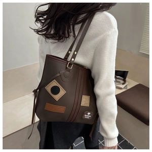 Detail view of large dark brown retro tote bag with shoulder straps worn by model