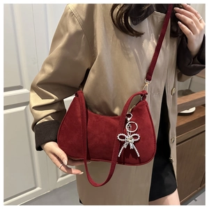 Detail of burgundy frosted half-moon bag with a silver bow charm worn over a beige coat