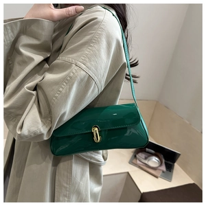 Detail of green patent leather baguette bag with gold lock worn with a beige trench coat
