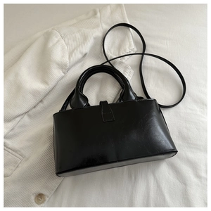 Top view of black leather bucket bag with dual handles on a white blazer background