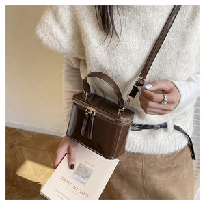 Brown box-shaped bag in glossy finish held by a model in a cozy winter knit sweater
