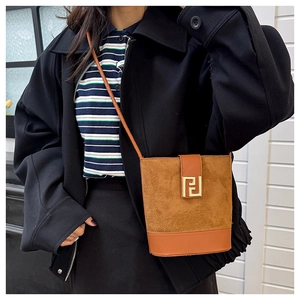 Detail view of brown suede bucket bag with gold geometric logo and leather shoulder strap