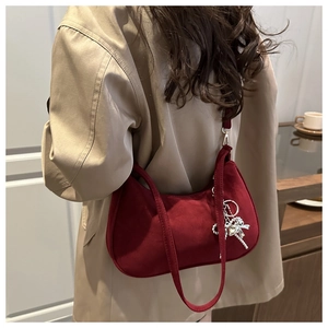 Dettaglio borsa a mezzaluna in camoscio rosso con ciondolo argento su blazer beige