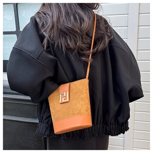 Detail shot of camel brown suede bucket bag featuring a prominent gold metal clasp design